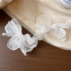 Close-up of elegant gold hoop earrings with delicate white organza fabric flowers.