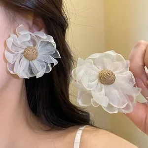 Dettaglio di grandi orecchini a fiore in chiffon bianco con centri in rafia su orecchio