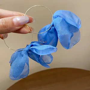 Detailed view of blue fabric petal flower gold hoop earrings held in hand