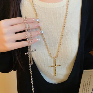 Close-up detail of retro metallic cross pendant on a stylish ball chain worn by model