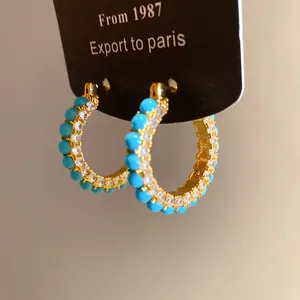 Close-up of gold hoop earrings with turquoise beads and clear zirconia detail