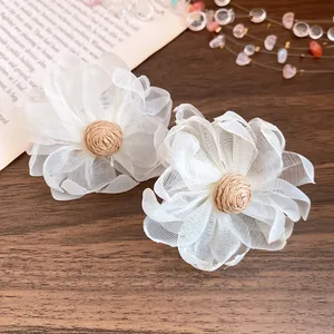 Dettaglio degli orecchini a fiore in chiffon bianco con centro in rafia per lo stile estivo.