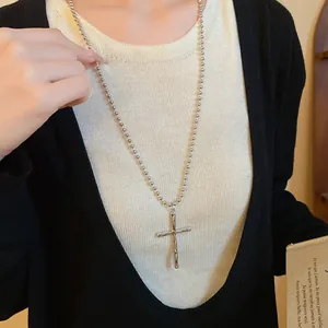 Close-up view of a vintage silver metal cross pendant necklace worn on a silver ball chain.