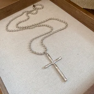 Detailed close-up of a vintage silver cross pendant on a classic beaded ball chain necklace
