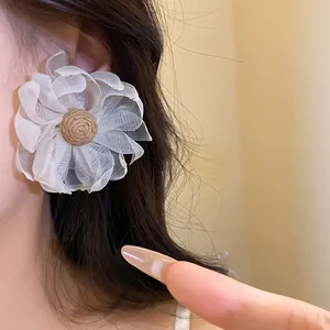 Dettaglio di grandi orecchini a fiore in chiffon bianco con centro in rafia per l'estate
