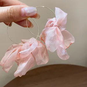 Hand-held detail of sweet pink fabric flower hoop earrings for women.
