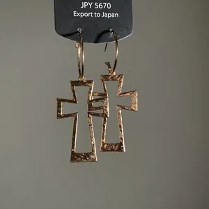 Detailed view of gold hollow cross earrings with hammered texture on black display card
