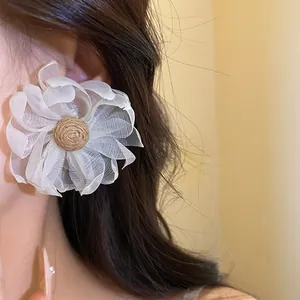 Primo piano di eleganti orecchini a fiore in chiffon bianco con centro in raffia su una modella