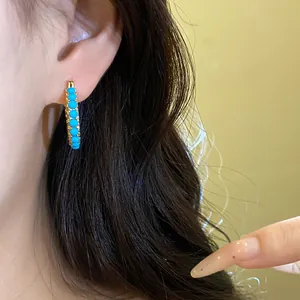 Close-up detail of a vintage gold hoop earring with turquoise beads on a model's ear.