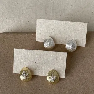 Close-up of teardrop zircon stud earrings featuring brushed gold and silver finishes