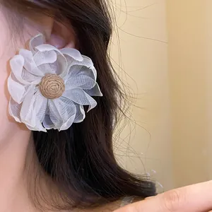Primo piano di orecchino a fiore in chiffon bianco con centro in paglia di rafia