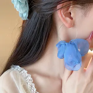 Close-up of blue fabric petal hoop earrings worn by a model for a sweet vacation look.