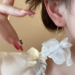 Detailed close-up of white chiffon flower hoop earring worn by a model in warm light