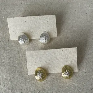 Close-up of gold and silver waterdrop earrings with zircon star on linen background