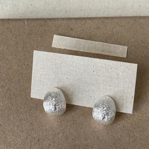 Macro view of silver teardrop stud earrings with zircon star pattern on textured cardstock