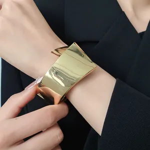 Detailed macro view of a wide gold-tone polished metal cuff bracelet worn on a model's wrist