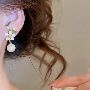Close-up detail of white enamel flower earrings with elegant round pearl drop pendant