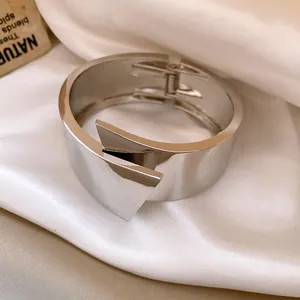 Close-up of minimalist silver geometric bangle with cross-over triangular design