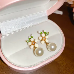 Close-up of elegant white enamel flower earrings with pearl drops in a pink jewelry box