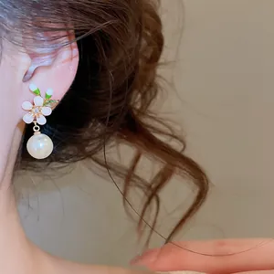 Close-up detail of vintage white enamel flower earring with a dangling lustrous white pearl