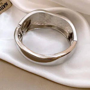 Macro view of a polished silver wide bangle featuring an elegant hinge and textured interior