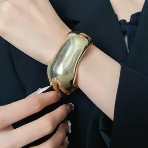 Detailed view of a wide glossy gold-tone fashion bangle on a wrist for a minimalist look