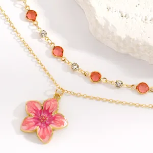 Close-up of gold-plated necklace with pink enamel flower and red crystal chain detail
