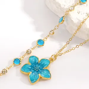 Macro view of a gold-plated necklace featuring a blue enamel flower and crystals