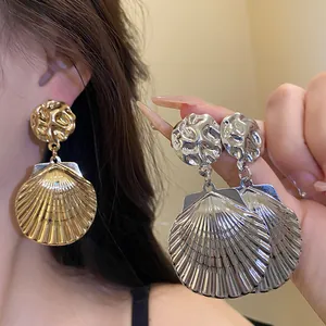 Detailansicht gold- und silberfarbener Ohrhänger in Muschelform mit Metallstruktur.