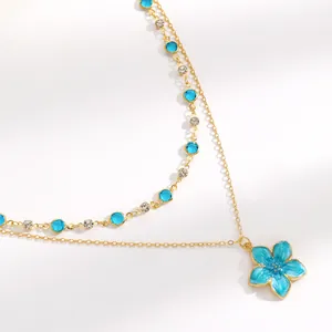 Close-up of double-layer gold chain necklace with blue enamel flower and crystals