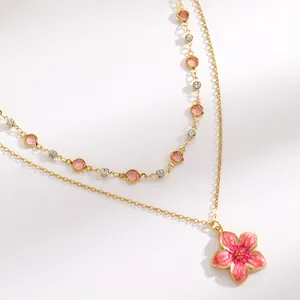 Close-up of double-layered gold necklace with pink flower pendant and crystals.