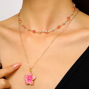 Close-up of a stylish gold layered necklace featuring a pink enamel flower and crystals