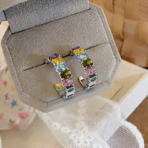 Macro view of colorful oval zirconia C-shaped earrings inside a grey velvet jewelry box