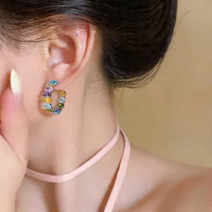 Close-up detail of colorful oval zircon C-shaped hoop earrings worn by a model