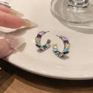 Close-up detail of multi-colored oval zircon C-shaped hoop earrings on ceramic plate