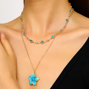 Close-up detail of double layered gold necklace with blue enamel flower and crystals