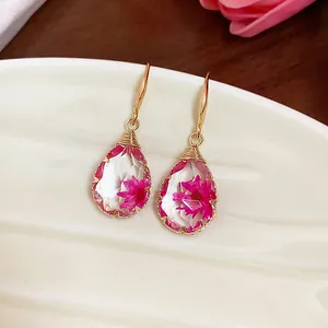 Primo piano di orecchini a goccia in resina con fiori secchi rosa e ganci dorati.
