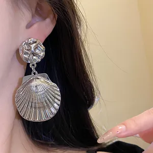 Detailaufnahme eines silbernen Muschel-Ohrrings mit elegantem Faltenmetall-Design