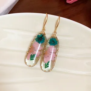 Eleganti orecchini ovali in resina con fiori rosa e blu e ganci dorati molto raffinati.