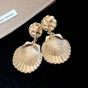 Nahaufnahme von goldenen plissierten Muschel-Ohrhängern mit Hochglanz-Metallfinish.
