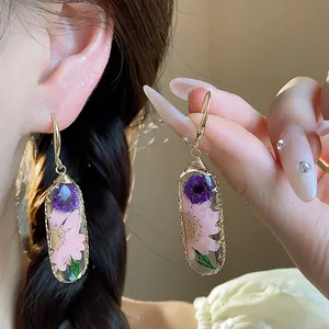 Dettaglio di orecchini in resina con fiori secchi viola e rosa incorporati a mano.