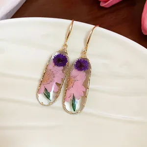 Vista dettagliata di eleganti orecchini in resina con veri fiori secchi rosa e viola