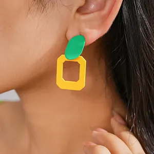 Primo piano di orecchini geometrici color block vibranti con finitura a spruzzo su modella.