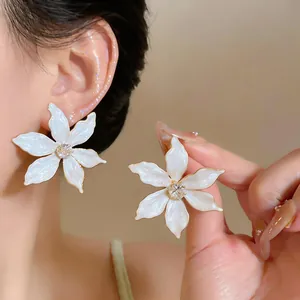 Detailed close-up of white enamel flower earrings with a sparkling zirconia center piece