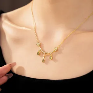 Detailed view of an 18k gold plated necklace with green zircons and flower design.