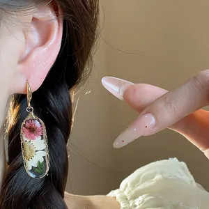 Dettaglio ravvicinato di orecchini in resina con veri fiori secchi rosa e bianchi