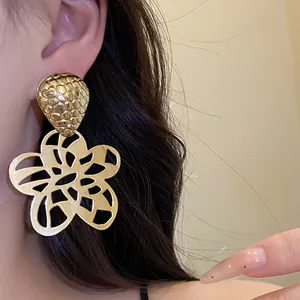 Makro-Detailansicht goldener hohler Blumen-Ohrhänger im Vintage-Stil an einem Modell-Ohr.
