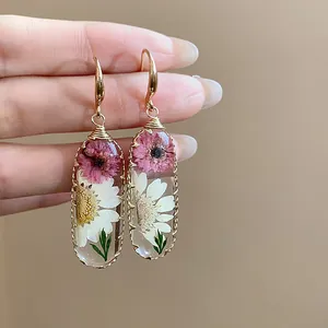 Primo piano di orecchini in resina fatti a mano con veri fiori secchi rosa e bianchi.