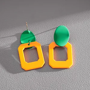 Primo piano di orecchini geometrici verdi e arancioni con aghi in argento su pelle.