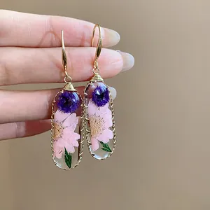 Dettaglio di orecchini a goccia in resina con fiori secchi rosa e viola veri